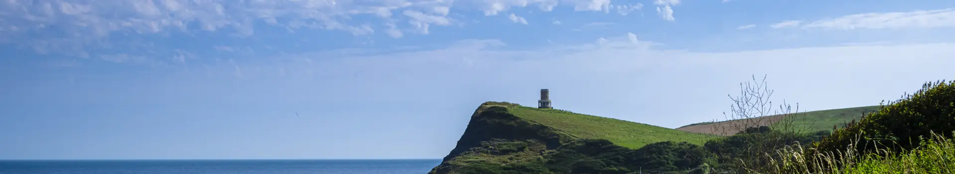a folly in a green field on a coastal path with the sea and sky behind