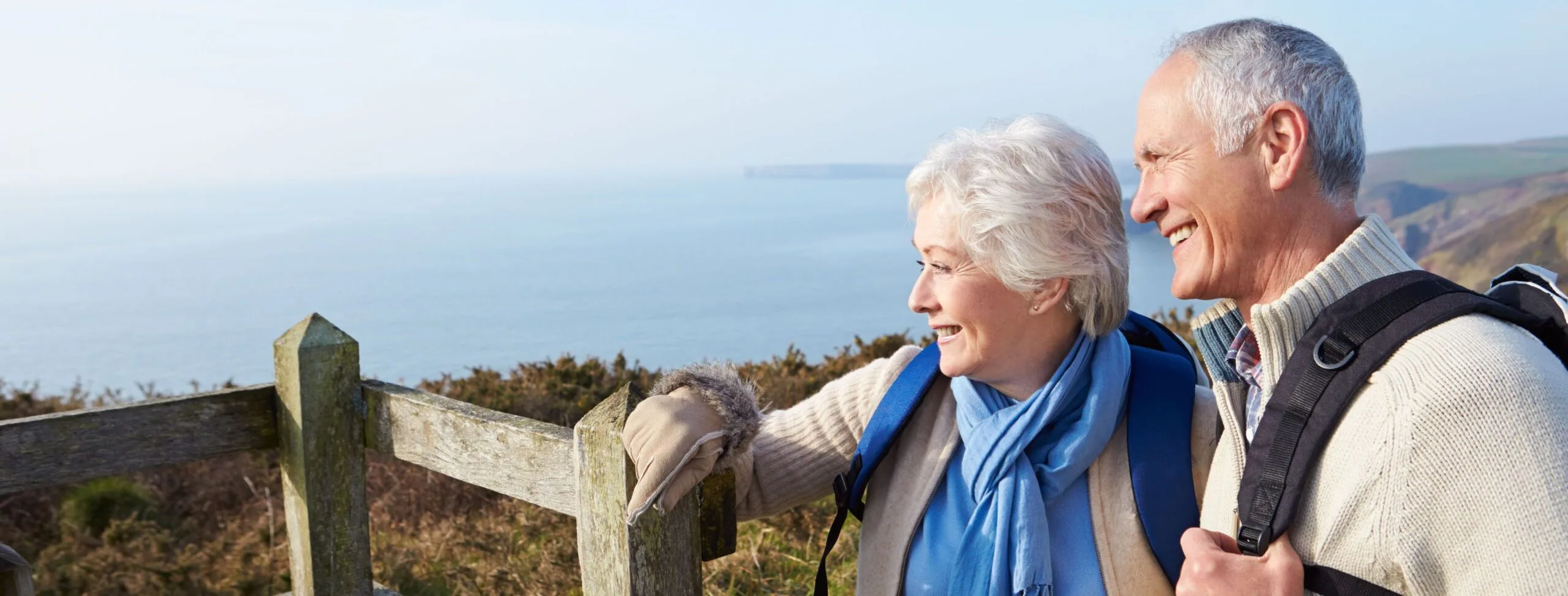 A happy couple in their 60s enjoying an autumn walk along the coastal path with the sea in the background